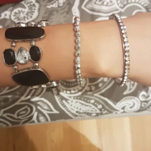 Tre snygga armband i silver och svart - Säljer tre armband: ett brett armband med svarta stenar och silverdetaljer, ett smalt armband med små silverfärgade pärlor och ett glittrigt armband med gnistrande stenar. Perfekt för dig som gillar att mixa olika stilar och vill ha något som sticker ut. PRIS KAN DISKUTERAS! 15 kr/st.