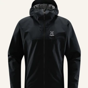 Svart regnjacka från Haglöfs - Svart regnjacka från Haglöfs med minimalistisk design och logga på bröstet. Jackan har huva, hel dragkedja och är tillverkad i syntetmaterial som står emot regn. Perfekt för blöta dagar och enkel att slänga på sig över en hoodie. Kom gärna med prisförslag!