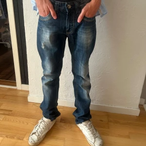 Nesal blå jeans med slitningar - Snygga blå jeans från Nesal med coola slitningar och tvättade detaljer. Klassisk femficksmodell med raka ben och kontrastsömmar. Jeansen har normal passform och är tillverkade i slitstarkt bomullstyg. Perfekta för en avslappnad streetstil.