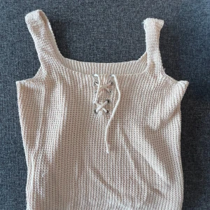 Beige stickad linnetopp med snörning - Snygg beige stickad linnetopp med breda axelband och cool snörningsdetalj framtill. 