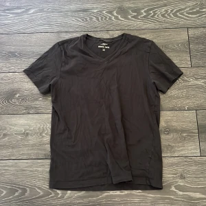 Svart v-ringad t-shirt H&M - En stilren svart t-shirt från H&M med v-ringning och korta ärmar. Tillverkad i mjuk bomull som känns skön mot huden. Perfekt basplagg att matcha med jeans eller shorts. Enkel och clean design utan tryck eller mönster.