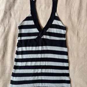 Randig svart och grå linnetopp - Snygg linnetopp med v-ringning. Toppen har horisontella svarta och gråglittriga ränder och är ärmlös. Perfekt för varma dagar och enkel att matcha med jeans eller shorts.