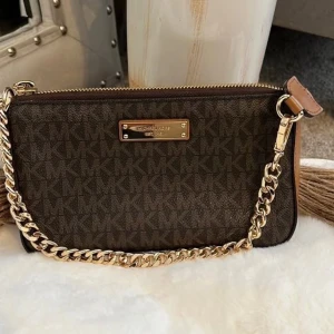 Brun Michael Kors axelväska med kedja - Snygg brun axelväska från Michael Kors med guldiga kedjedetaljer och klassiskt MK-mönster över hela väskan. knappppt använd äkta. 1500 på zalando