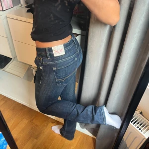 Mörkblå bootcut jeans från Tommy Hilfiger - Snygga mörkblå jeans från Tommy Hilfiger med klassiska kontrastsömmar och låg midja. Modellen har bootcut-ben och coola detaljer på bakfickorna. Jeansen är i stretchigt denim som sitter riktigt bra. Liknar true religion jeansen! Modellen heter ”Nikita straight” storlek: W26 L32🩷
