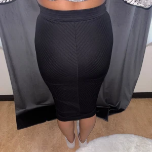 Svart tight kjol med dragkedja - Säljer en svart, tight kjol med snygg struktur och dragkedja framtill. Kjolen är midilång och har ett diskret mönster i tyget som ger en cool look. Perfekt för dig som gillar en stilren och edgy vibe.