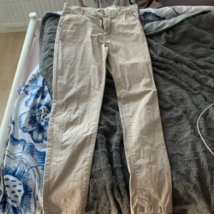 Beige chinos från L.O.G.G. i bomull - Snygga beige chinos från L.O.G.G. i mjuk bomull. Klassisk rak passform med bälteshällor, fickor fram och bak samt dragkedja och knapp. Perfekta för en clean och avslappnad stil.