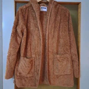 Beige teddyjacka med huva - Supermjuk och fluffig teddyjacka i beige färg. Jackan har huva, två stora fickor framtill och långa ärmar. Jätte mysig och bekväm :)