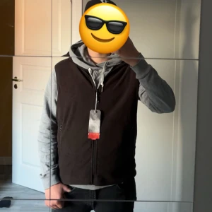 Brun/svart fleece väst - Svart väst från Ecogozz med hel dragkedja framtill och hög krage. Helt ny, jag är 1,75. Västen har en clean look utan mönster och är tillverkad i ett mjukt material som känns bekvämt. Perfekt att slänga över en hoodie för en chill stil.
