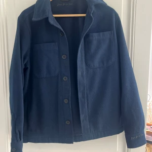 Mörkblå overshirt från Donce De La Sense - Overshirt i mörkblått från Donce De La Sense med klassisk krage, två stora bröstfickor och knäppning framtill. Storlek XS 