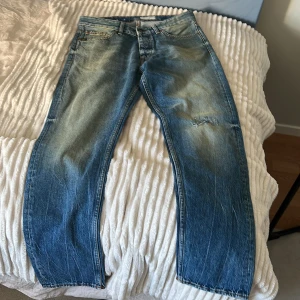 Blå jeansbyxor - Snygga blå jeansbyxor med en klassisk femficksdesign och slitna detaljer. De har en knappgylf och bälteshällor, vilket ger en tidlös look. Perfekta för en avslappnad stil.