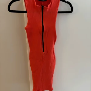 Orange ribbad klänning med dragkedja - Snygg orange ribbad klänning från Naked Wardrobe med dragkedja framtill. Den är ärmlös och har en tight passform som framhäver figuren.