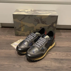 Valentino Rockrunner sneakers i grå och blå - Snygga Valentino Rockrunner sneakers i en mix av grått och blått med svarta detaljer. Skorna har en cool camouflagemönster och en robust sula med nitar. Perfekta för en stilren look.   (BYTE TILLGÄNGLIG)