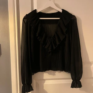 Svart blus från Zara  - En svart blus från Zara med v-ringad hals. Räfflor vid handleden och längs med v-ringningen. Super snygg till sommaren och passar jättebra till lite finare tillställningar. Storlek m.