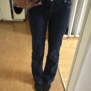 Mörkblå bootcut jeans - Snygga mörkblå bootcut jeans med hög midja och klassisk femficksdesign. Jeansen har en dragkedja och knapp framtill samt dekorativa sömmar på bakfickorna. Perfekta för en stilren look.