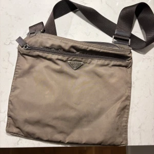 Grön/brun axelväska från Prada - Snygg grön/bron axelväska från Prada med justerbar axelrem. Väskan har en stilren design med en diskret logotyp på framsidan. Perfekt för att bära dina dagliga nödvändigheter med stil. (I använda skick, 7/10)