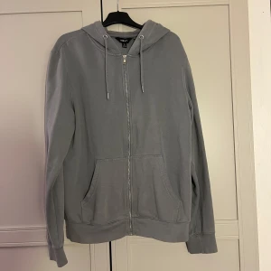Grå hoodie från NEXT - Säljer en stilren grå hoodie från NEXT med dragkedja och justerbar huva. Tröjan har långa ärmar och praktiska fickor framtill. Perfekt för en avslappnad look.