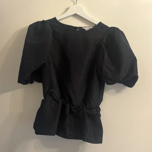 Svart blus med puffärmar - Elegant svart blus med korta puffärmar och rund hals. Perfekt för en stilren look.