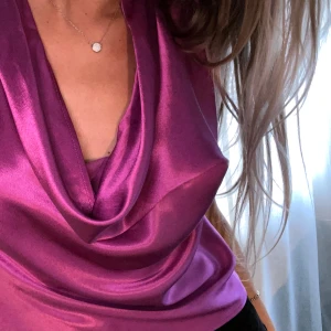 Fuschia/lila satinlinne från Zara - Ärmlös satintopp med draperad halsringning. Köpt på Zara, i storlek S. 100% viskos. Säljes i nyskick! Toppen är oanvänd och prislappen sitter kvar. Mått: längd 50 cm, midjevidd: 90 cm. 💕