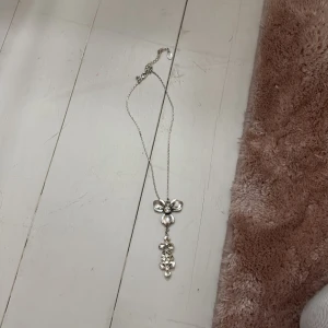 Silverfärgat halsband med blommor - Elegant silverfärgat halsband med ett hängsmycke i form av blommor. Halsbandet har en justerbar kedja och blommorna är dekorerade med små glittrande stenar. Perfekt för att ge en stilfull touch till din outfit.