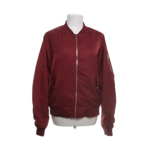 Vinröd bomberjacka - Snygg vinröd bomberjacka med dragkedja framtill. Jackan har långa ärmar och ribbade muddar vid ärmslut och nederkant. Perfekt för en cool och avslappnad stil. Varan har tecken på användning. Defekter förekommer säg till så skickar jag bild. Storlek L men sitter som en S/M