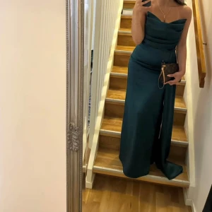 Mörkgrön axelbandslös långklänning - Elegant mörkgrön axelbandslös långklänning. Endast använd en kväll. I mycket bra skick. För referens är jag 163 cm och det är storlek S.