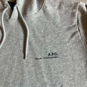 Grå hoodie från A.P.C. - Säljer en stilren grå hoodie från A.P.C. med tryck på bröstet. Tröjan har en klassisk design med huva och dragsko samt ribbade muddar vid ärmslut och nederkant. Perfekt för en avslappnad look. Tröjan är i storlek S men passar XS nypris ligger på 2999kr mitt pris 999kr.