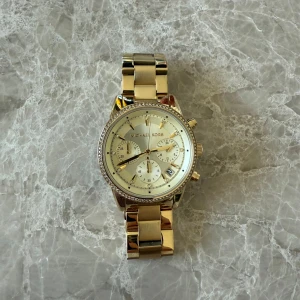 Guldfärgad klocka från Michael Kors - Guld klocka från Michael Kors med diamantkant runt uret. Knappt tecken på användning, nypris 2 695 kr 