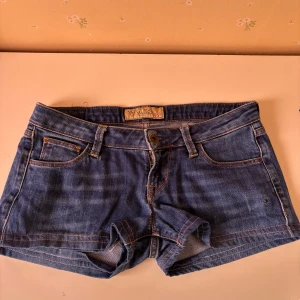 Blå jeansshorts från Guess - Snygga lågmodjade blå jeansshorts från Guess med klassisk femficksdesign och knappgylf. Perfekta för varma sommardagar. De har en lågmidjad passform som ger en avslappnad look.
