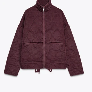 Vinröd quiltad jacka - Snygg vinröd quiltad jacka med dragkedja och hög krage. Jackan har en loose passform och är perfekt för kyligare dagar. Den har långa ärmar och justerbar dragsko i nederkant för extra stil och komfort.