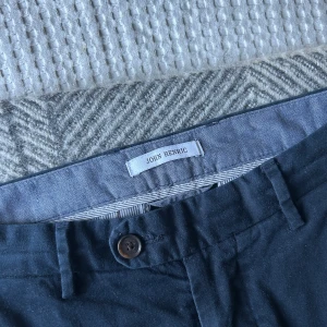 Blåa chinos från John Henric - Snygga blåa chinos från John Henric med knapp och dragkedja i midjan. Byxorna har en klassisk design med sidofickor och en bakficka med knapp. Perfekta för en stilren look.