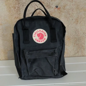 Svart ryggsäck från Fjällräven Kånken - Säljer en klassisk svart ryggsäck från Fjällräven Kånken. Den har ett stort huvudfack, en mindre framficka och två sidofickor. Väskan har dubbla handtag och justerbara axelremmar. Perfekt för både skola och utflykter!