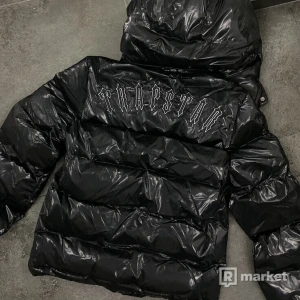 Svart pufferjacka från Trapstar kvitto finns - Säljer en svart pufferjacka från Trapstar med glänsande yta och logotyp på ryggen. Jackan har långa ärmar och är tillverkad i 100% polyester. Perfekt för att hålla värmen med stil.
