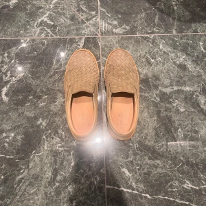 Beige loafers med flätad design - Snygga beige loafers med en unik flätad design. Perfekta för en stilren look och bekväma att bära hela dagen. Passar bra till både avslappnade och mer uppklädda tillfällen.