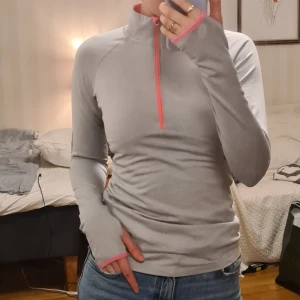 Grå långärmad träningströja med dragkedja - Grå långärmad träningströja som passar både för träningspass på gymmet eller som lager två när det är kallt. Tröjan har använts en del men det syns inte mycket förutom på ettiketten som suddats ut efter några tvättar.