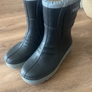 Svarta power boots från Polyver - Säljer ett par svarta vinterstövlar från Polyver med grå sula och foder. Stövlarna har en robust design med bra grepp på sulan, perfekt för kalla och hala dagar. De är vadderade för extra värme och komfort.