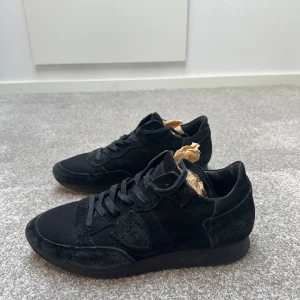 Svarta sneakers från Phillipe model  - Snygga svarta sneakers från Phillipe model i mocka och syntet. Skorna har en stilren design med snörning och en diskret look som passar perfekt för en trendig stil.