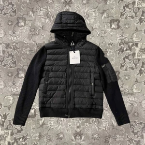 Svart jacka från Moncler - Snygg svart jacka från Moncler med quiltad design och huva. Jackan har dragkedja framtill och ribbade ärmar. Perfekt för kyligare dagar.