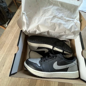 Nike Air Jordan 1 Low G i svart och grå - Säljer ett par Nike Air Jordan 1 Low G i svart och grå. Skorna har en klassisk design med snörning och en stilren look. Perfekta för både vardag och sportiga aktiviteter. Pris går att diskutera!!!