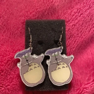 Totoro örhängen - Charmiga örhängen med Totoro-motiv. De har en tecknad stil med ljusa färger och är perfekta för fans av Studio Ghibli. Hängena är fästa på krokar för enkel användning.