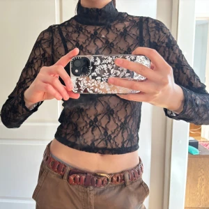 Svart spetsblus - Säljer en elegant svart spetsblus med hög krage och långa ärmar. Blusen är genomskinlig och har ett vackert blommönster. Perfekt för att lägga till en touch av stil till din outfit.
