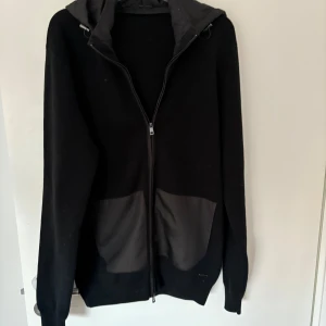 Svart jacka med huva - Säljer en svart cardigan med dragkedja och huva. Jackan har långa ärmar och två stora fickor framtill. Perfekt till våren