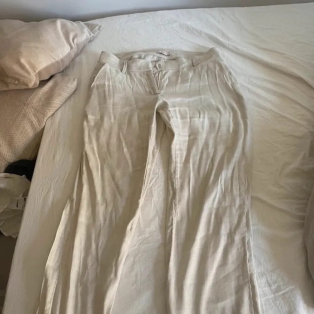 Snygga beige linnebyxor med hög midja och rak passform. Perfekta för en avslappnad stil. Byxorna har bälteshällor och en enkel design som gör dem lätta att matcha med olika toppar.. Farkut & Housut.
