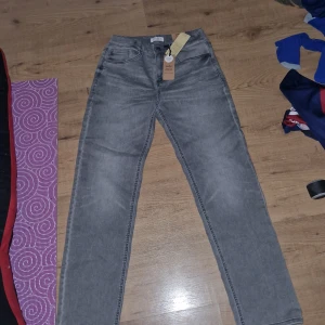 Grå jeans från Lindex - Säljer ett par grå jeans från Lindex med rak passform och normal midja. Byxorna är tillverkade i en återvunnen bomullsblandning och har en superstretchig jersey. Perfekta för en avslappnad stil.