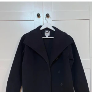 Navy kappa med knappar - Snygg navy kavaj med stora knappar framtill och bred krage. Perfekt för en stilren look. Passar bra till jeans eller mer formella byxor.