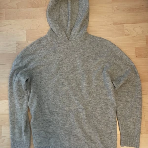 Grå Merinoull hoodie - Säljer en stilren grå merinoull hoodie med långa ärmar. Perfekt för kyliga dagar med sin mjuka och bekväma passform. Den har en klassisk design utan extra detaljer, vilket gör den lätt att matcha med olika outfits.
