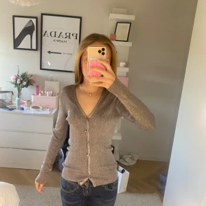 Glittrig grå kofta från Kookai - Säljer en snygg glittrig grå kofta från Kookai. Den har en v-ringad design med knappar framtill och långa ärmar. Perfekt för att lägga till lite glitter i din outfit! Har aldrig används.