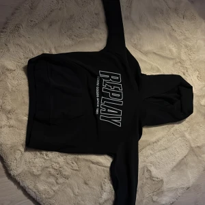 Svart hoodie från Replay - Säljer en svart hoodie från Replay med stor logga på framsidan och en mindre logga på ärmen. Tröjan har en klassisk känguruficka och en bekväm huva. Perfekt för en avslappnad stil.