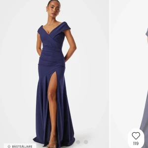 Marinblå långklänning med slits - Elegant marinblå långklänning med en djup v-ringning och slits framtill. Klänningen har en offshoulder-design som ger en sofistikerad look. Perfekt för speciella tillfällen.