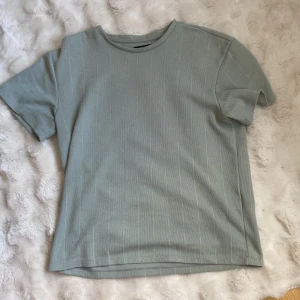 Grön t-shirt från Jack & Jones - Säljer en stilren grön t-shirt från Jack & Jones. Den har ett diskret randigt mönster och är tillverkad i en mjuk bomullsblandning. Perfekt för en avslappnad look.