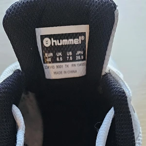 Vita sneakers från Hummel - Snygga vita sneakers från Hummel med svarta detaljer och snörning. Skorna har en rund tå och en slitstark sula i gummi. Perfekta för en aktiv livsstil och ger bra grepp på olika underlag. Min son har använt dom ett fåtal gånger som inneskor i badminton.
